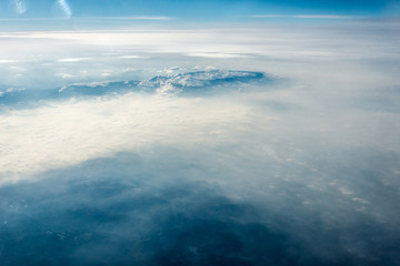 Top view of white clouds between which you can see high mountains