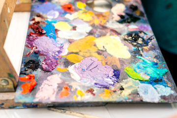 Paints of different colors on a multi-colored palette of mixed oil paints