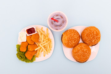 Fast food dish top view. Meat burger, potato chips and wedges. Take away composition. French fries, hamburger, nagets and soda on blue background.