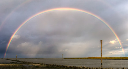 Ein eindrucksvoller Regenbogen über dem Wattenmeer von Bensersiel mit Wangerooge am Horizont