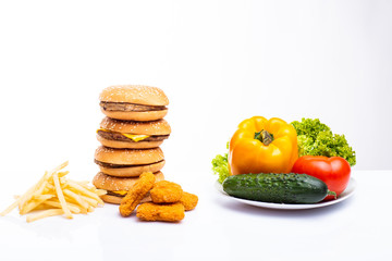 Concept of healthy and unhealthy food. Vegetables vs fast food, burgers, nagets and french fries isolated on white background