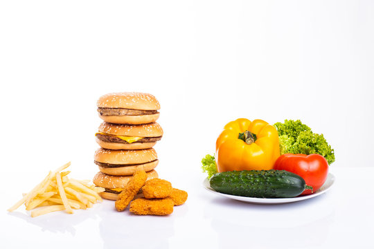Concept of healthy and unhealthy food. Vegetables vs fast food, burgers, nagets and french fries isolated on white background