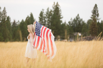 Beautiful young woman holding flag above head in field