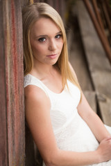 Attractive young woman sitting against old red wood barn looking at camera