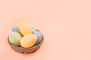 Flatlay with dyed on green, yellow and grey Easter eggs in the straw basket isolated on peach...
