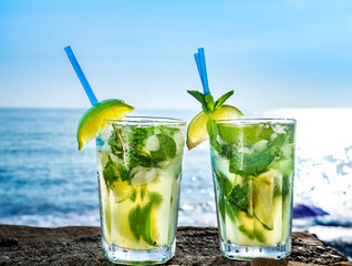 Cocktail mojito with ice and lemon in two glasses on the background of the ocean closeup
