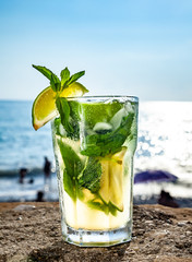 Cocktail mojito with ice and lemon on the background of the ocean closeup