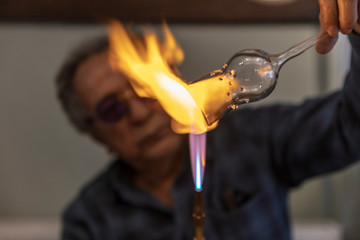 Close up macro of glass blower working with flame on a handmade wine glass from precious crystal in...