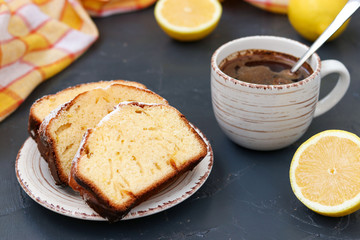 Lemon muffin arranged on a plate against a dark background with a cup of coffee in the background