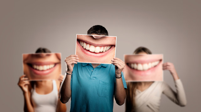 three happy people holding a picture of a mouth smiling on a gray background