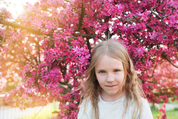 Beautiful pretty blond little girl smelling flowers in blooming sakura garden. 