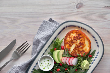 Fried round slice of cheese with green rucola salad with avocado, radish and pomegranate seeds