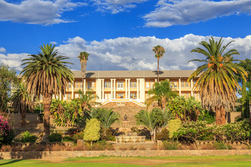 Fototapeta na wymiar Park and garden with yellow palace building hidden behind tall palms, Windhoek, Namibia