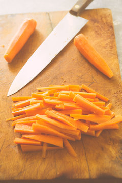 Carrot sticks, cut on a cutboard with a big knfe, ready to be prepared as typical italian "pinzimonio", pouched on olive oil and rosmery,vertical composition, topview flatlay.
