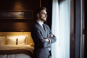 Young handsome man relaxing at his apartment in a hotel after business meeting. Business trip. Booking hotel during your vacation. Businessman in luxury room  of the expensive beautiful hotel.