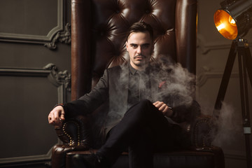 Young handsome man posing for a fashion shoot in a studio. Fashion as a lifestyle. Man wearing a beard. Model sitting on a sofa in tuxedo. Successful fashionable businessman. Business look advertising