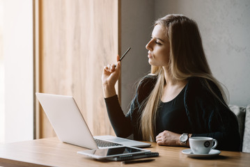 Beautiful girl working out a plan of the project and concept. Girl paints a website design on a laptop. student prints a message on the phone in the messenger. Development. Digital marketing