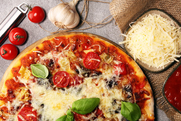 Vegetarian Italian pizza with melted cheese, red tomatoes and green basil on a table decorated by...