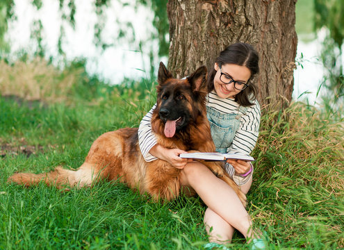 Portrait of young beautiful woman sitting with book and hugging her German Shepherd dog. Happiness and friendship. pet and woman. Summer concept