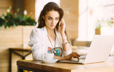 Beautiful girl working out a plan of the project and concept. Girl paints a website design on a laptop. student prints a message on the phone in the messenger. Development. Digital marketing