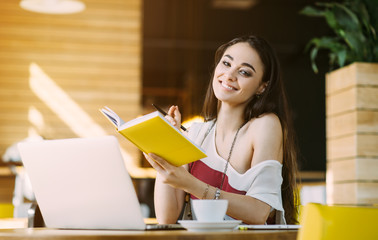 Beautiful girl working out a plan of the project and concept. Girl paints a website design on a laptop. student prints a message on the phone in the messenger. Development. Digital marketing