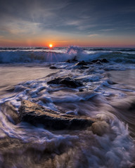 Waves crashing in front of the setting sun with blue and orange sky. Photo by: Chuck Beyer