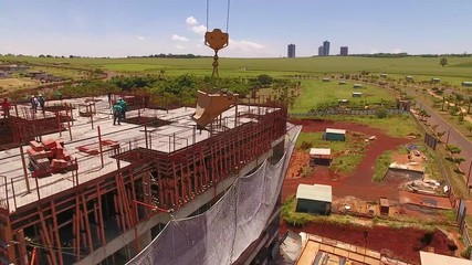 Concrete being raised by a crane to the top of a building. Several professionals working on the construction project. - Powered by Adobe