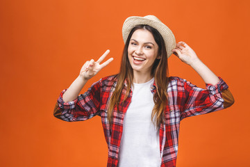 Obraz na płótnie Canvas Carefree gorgeous dreamy traveller in trendy beige head wear casual, so hot, fit and slim. Relax, rest, chill mode! Isolated over orange background. V-sign.