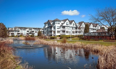 Fototapeta na wymiar Residential District in Richmond City with pond and fountain, blossom of sakura, green grass bushes and trees in the territory of residential complex, Vanсouver, British Columbia 