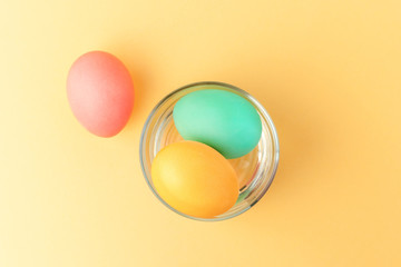 Bright creative Easter decoration of colorful eggs in a glass on vibrant yellow background. Top view.