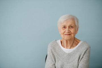 Portrait of elderely grey haired woman in a comfortable sweater at home - obrazy, fototapety, plakaty