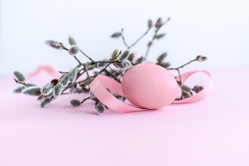 Palm sunday decoration of pussy willow with pink colored Easter egg and silk ribbon on light pink background. Close-up.