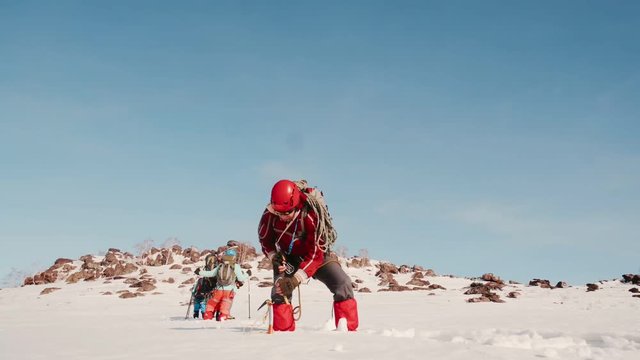 man climber unhooks the rope with a carbine from the icebreaker stuck in the thick snow. in the background is a group of climbers and a mountain hill.