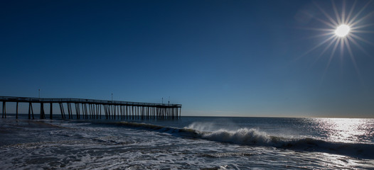 Obraz premium Waves crashing on the shore by a long ocean pier. Photo by: Chuck Beyer