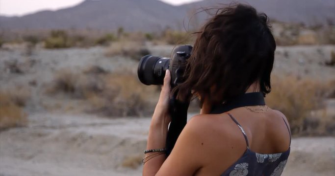 stylish female photographer brings camera up to face to  take photos out in the desert