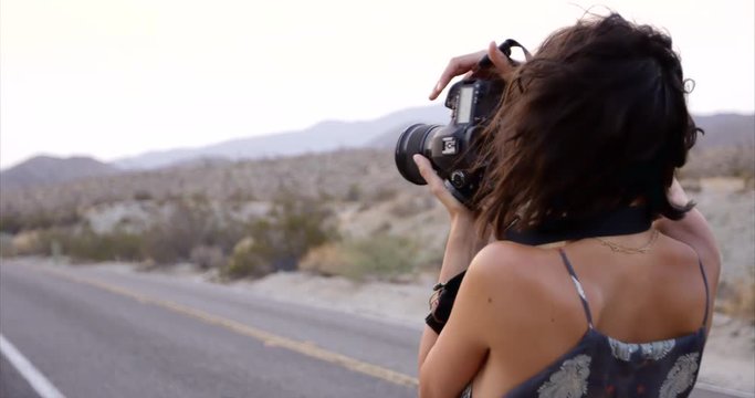 Stylish female photographer taking photos along desert highway - side profile