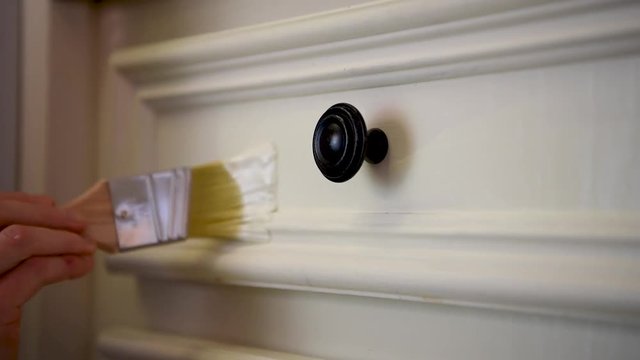 Close-up woman hand painting a white kitchen cabinet, detailed paint job around cabinet knob