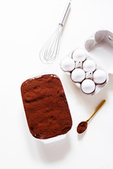 Preparing a tasty tiramisu , step by step visual guide, second lay of cream is pored followed by a sprinkle of chocolate powder as the final retouch for the perfect tiramisu cake,on a white board, top