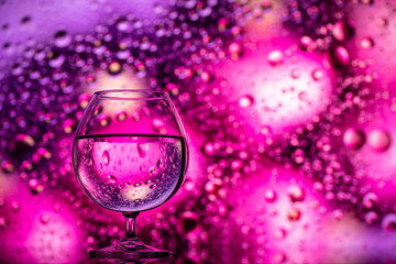 clear glass with water and oily drops on colored background