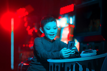 Fototapeta premium The child plays mobile games. The boy holds the phone in his hands. Neon lighting. Mobile games.