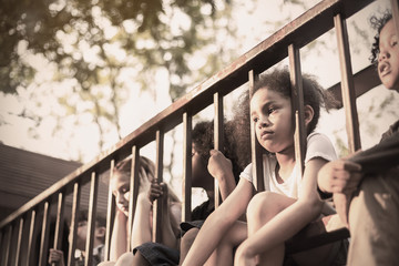 Multicultural little children sitting behind the fence. Homeless orphan stressful kids, education...