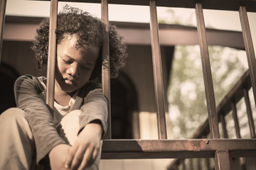 Little boy sitting behind the fence. Homeless orphan stressful kids, education sickness human right...