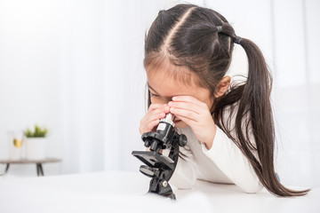Beautiful asian little girl looking at a microscope in a classroom. Selective focus on microscope. Education science project concept