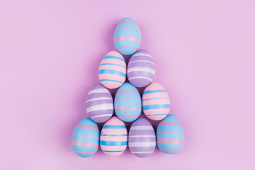 Pyramid of dyed on blue, pink and violet Easter eggs isolated on purple background. Easter theme flatlay.