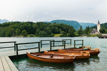 Naklejka na ściany i meble 21 June 2018 Slovenia Four wooden boats on moored on a wooden pier Beautiful mountain view Selective focus