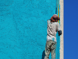 a man paints a wall in blue outdoors. back view