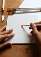 Hand of a female artist holding a white paintbrush for watercolour with empty canvas board