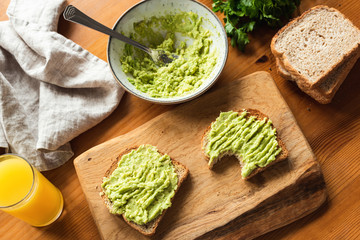Breakfast toast with mashed avocado on wooden cutting board and glass of orange juice. Healthy vegetarian breakfast