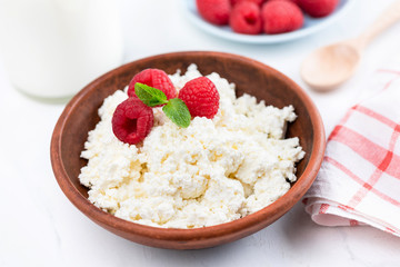 Bowl of cottage cheese, tvorog or curd cheese with fresh raspberries on white table. Rich in Calcium healthy dairy product