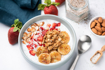 Smoothy bowl with banana, strawberry, granola, nuts on white table. Closeup view. Concept of healthy vegetarian diet, weight loss, balanced diet